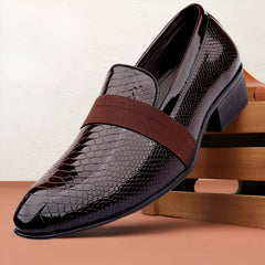 Brown leather dress shoe with a brown strap on a wooden surface