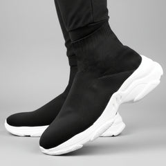 Black sock shoes with white soles worn by a person on a dark background