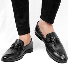 Black loafers with tassels worn with black checkered pants on a white background