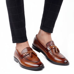 Brown leather loafers with tassels worn with black checkered pants on a white background
