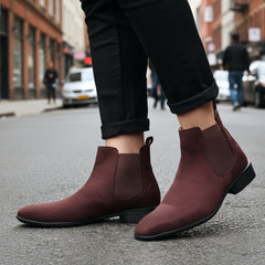 Brown Chelsea boots worn with black pants on a neutral background