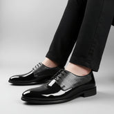 Black patent leather shoes with silver mesh accents worn by a person on a wooden floor.