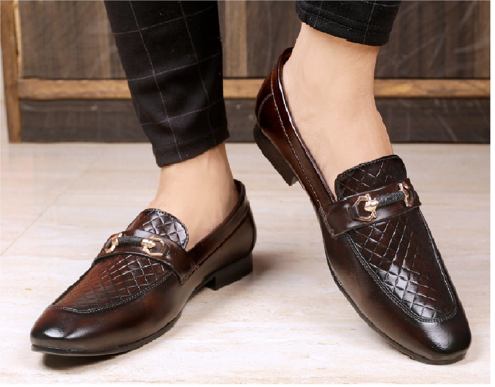 Brown leather shoes with decorative buckles worn by a person on a wooden floor.