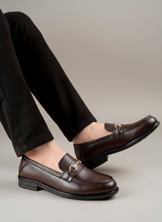 Brown loafers with gold accents worn by a person on a wooden floor.