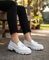 White loafers worn by a person sitting on a textured surface.