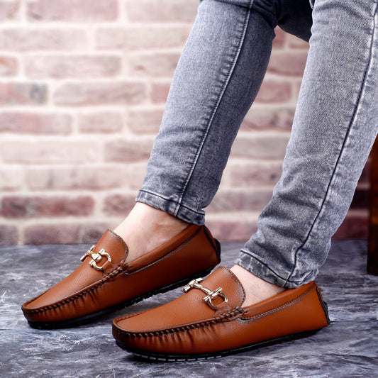 Brown loafers worn with gray jeans against a brick wall background