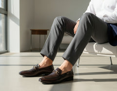 Brown leather shoes with decorative buckles worn by a person on a wooden floor.