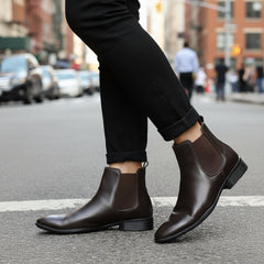 Brown leather Chelsea boots worn with black pants on a light background