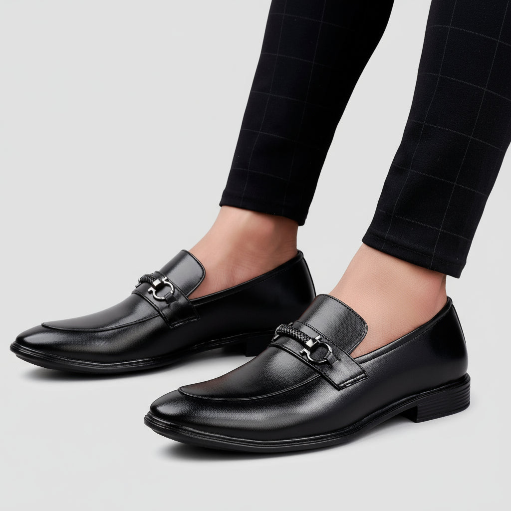 Black dress shoes worn with black pants on a wooden floor.