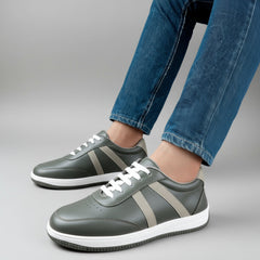Gray sneakers with white soles worn with blue jeans on a neutral background