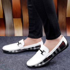 White loafers with black and red checkered soles worn by a person on a wooden floor.