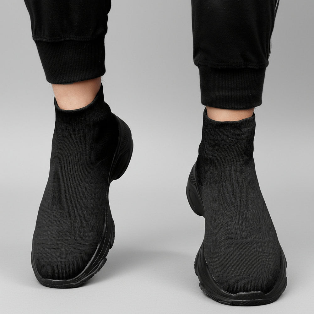 Black ankle boots worn with black pants against a dark background
