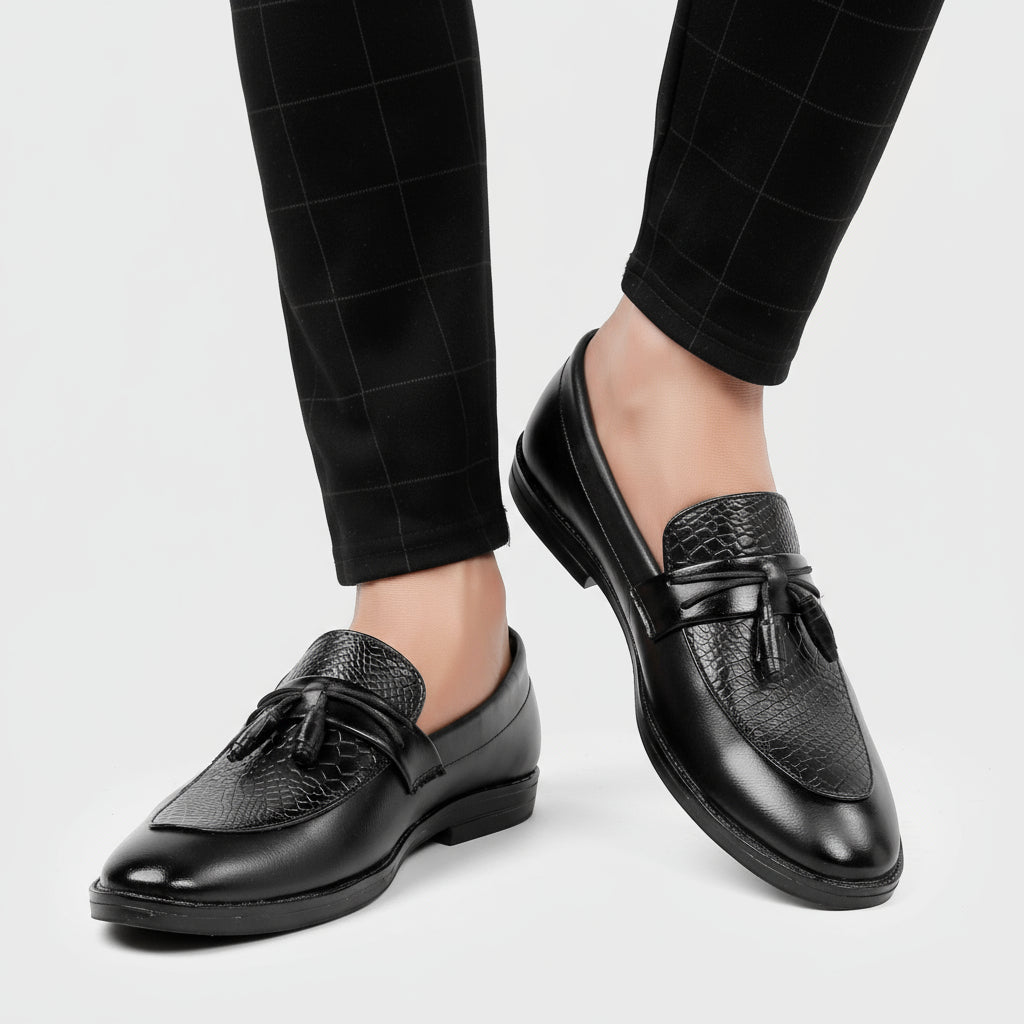 Black leather loafers with tassels worn with black pants on a white background