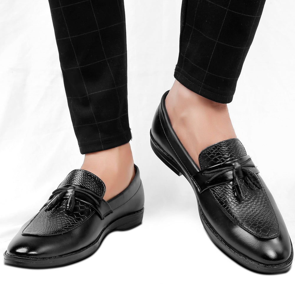 Black loafers with tassels worn with black checkered pants on a white background