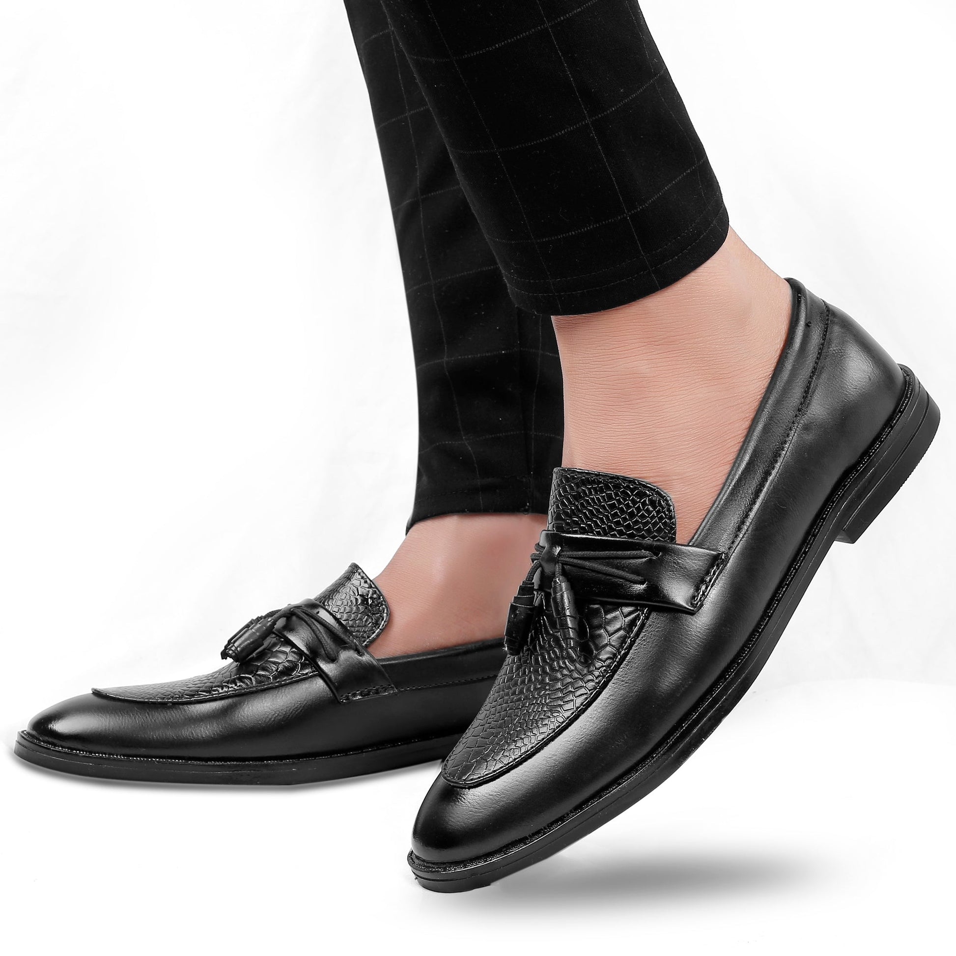 Black leather loafers worn with black pants on a white background
