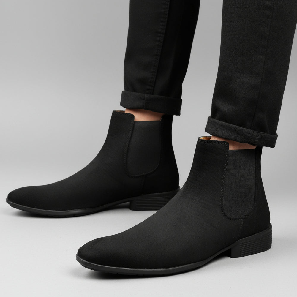 Black Chelsea boots worn with black pants against a neutral background