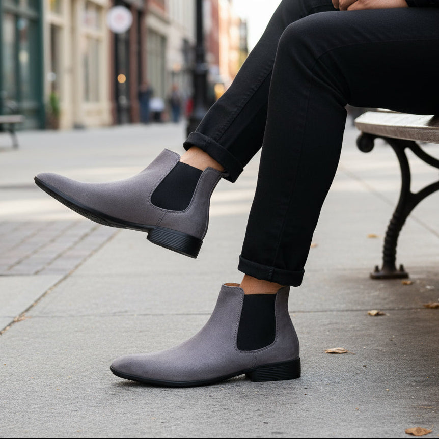 Gray suede Chelsea boots worn with black pants on a textured surface.