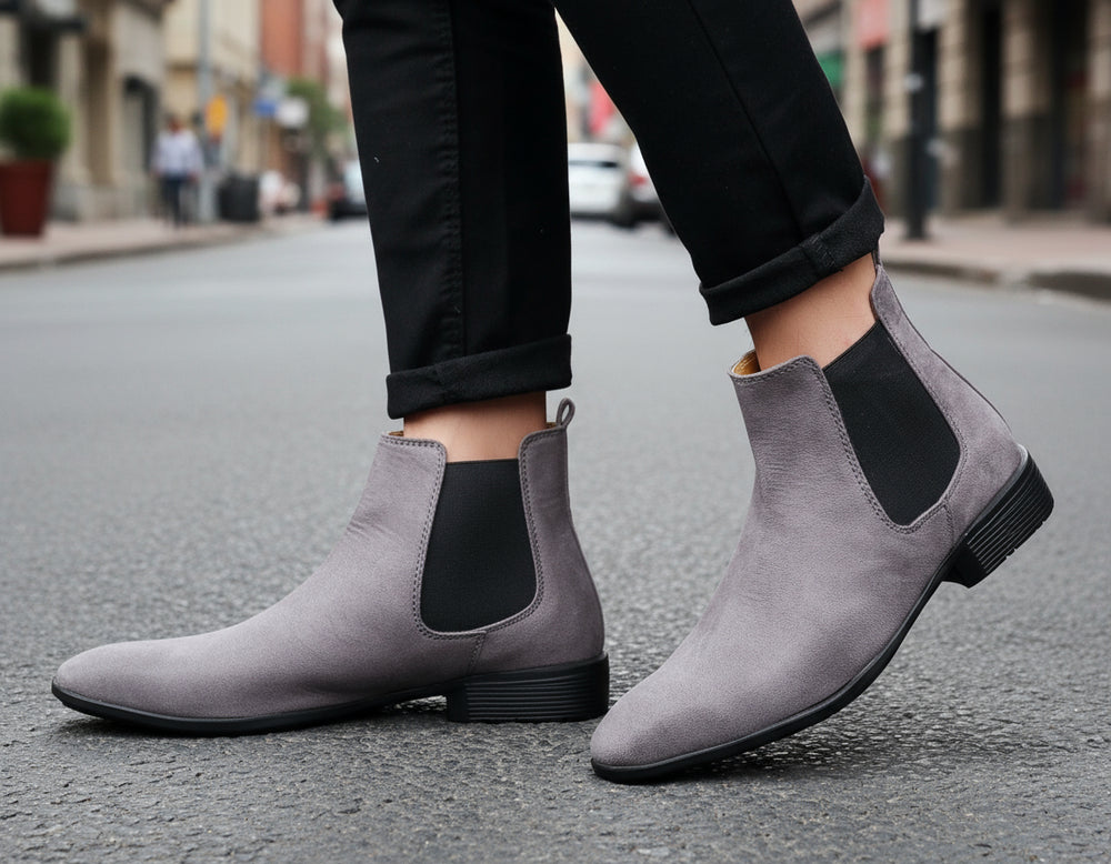 Gray Chelsea boots worn with black pants against a neutral background
