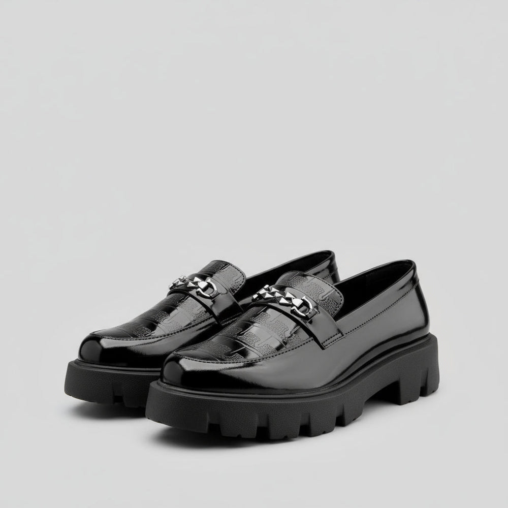 Black loafers with chunky soles on a yellow and white background, featuring the Buxy brand.