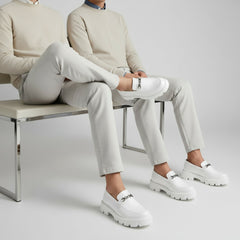 White loafers with chunky soles on a gray and beige background, featuring the Buxy brand.