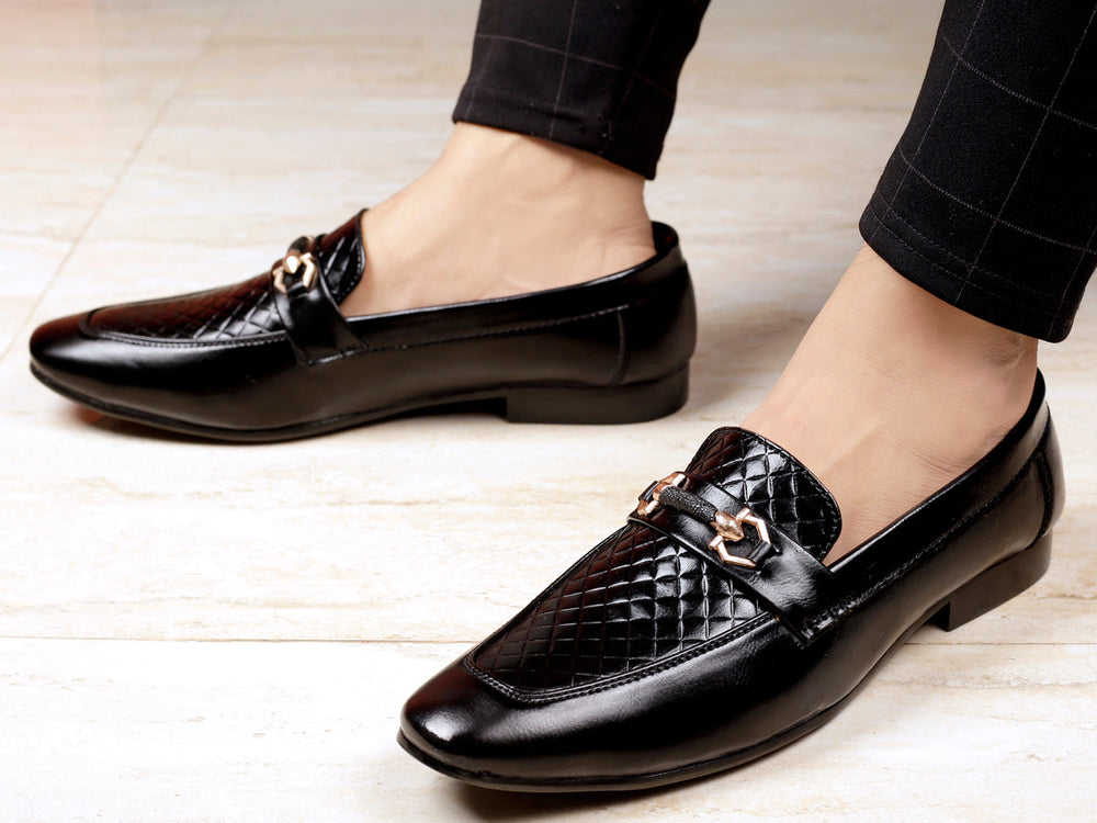 Black dress shoes with a quilted design worn by a person on a light wooden floor.
