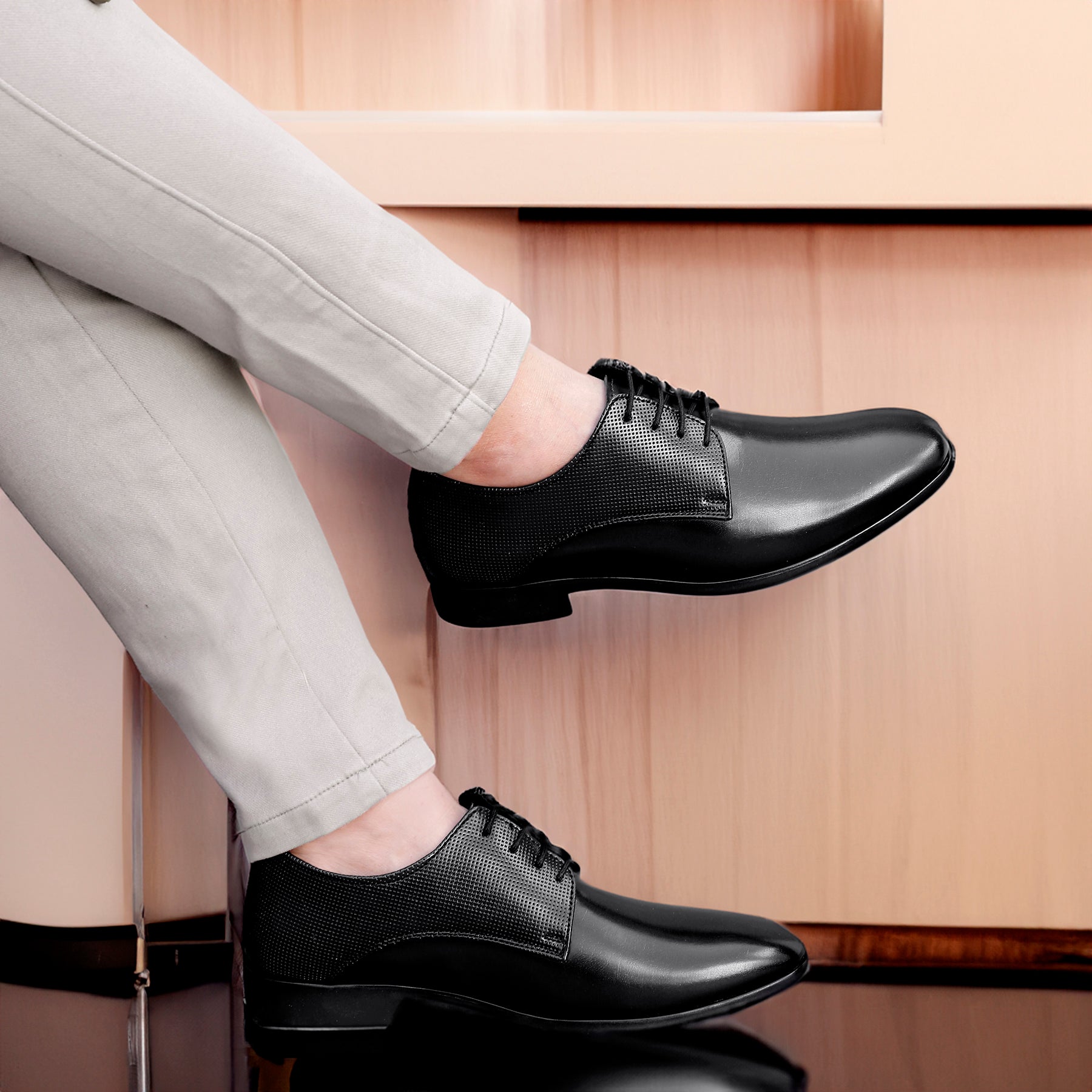 Black dress shoes worn with light gray pants on a wooden floor.