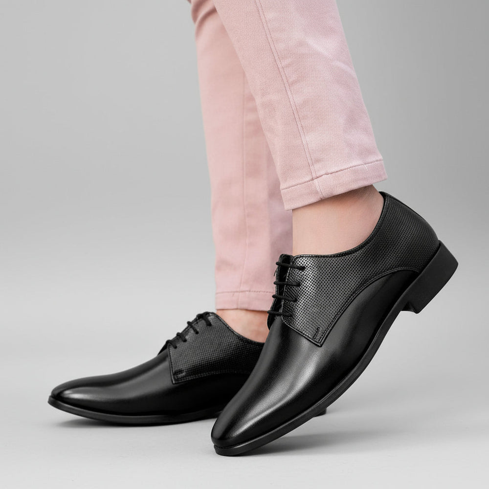 Black dress shoes worn with light pink pants on a blurred background