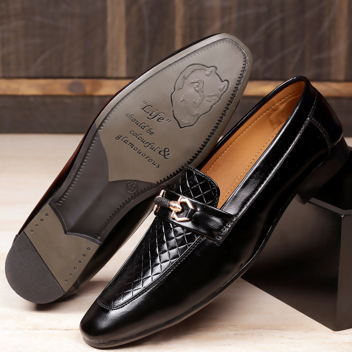 Black leather loafer shoe with a brand logo on a wooden surface