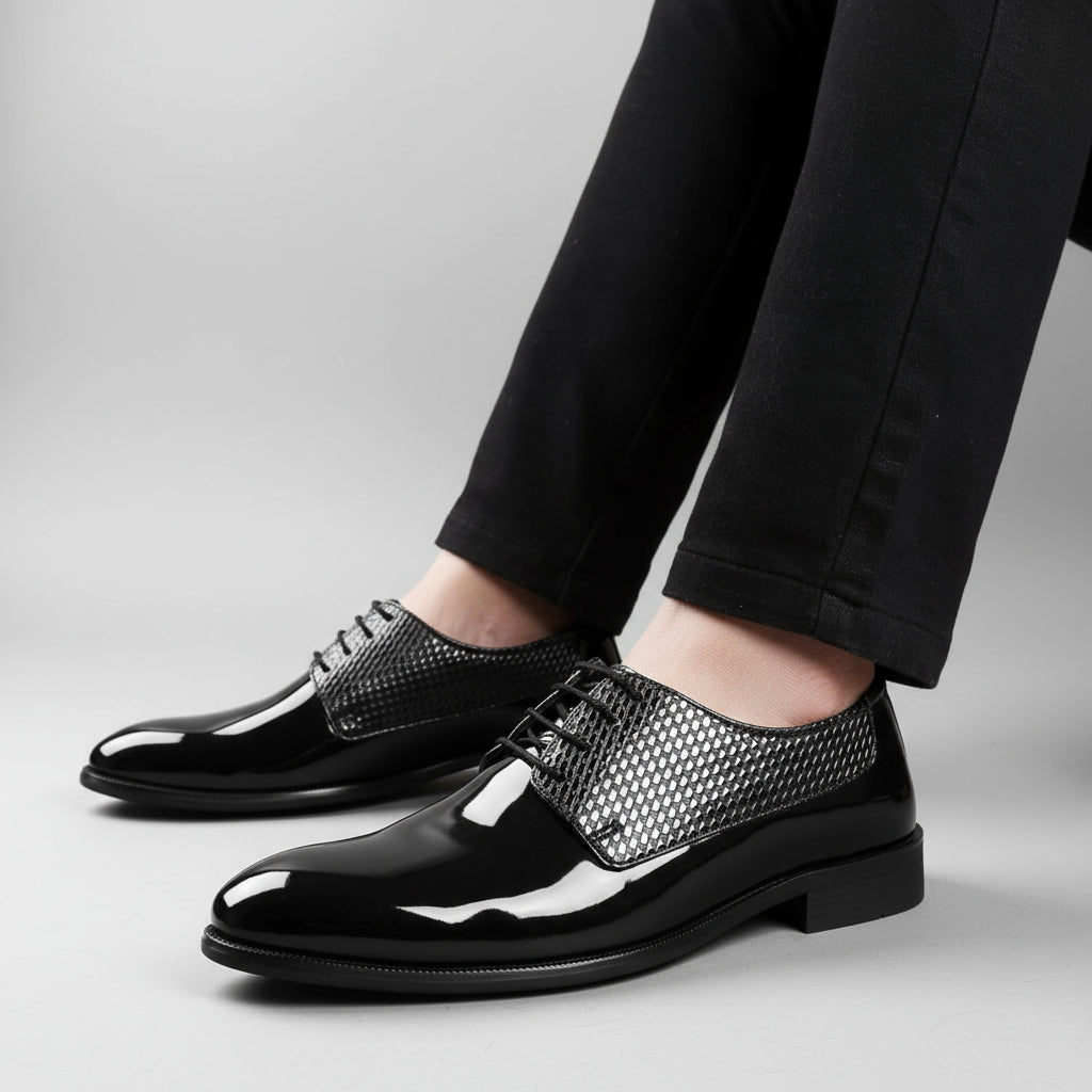 Black patent leather shoes with silver mesh accents worn by a person on a wooden floor.