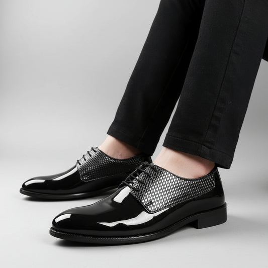 Black patent leather shoes with silver mesh accents worn by a person on a wooden floor.