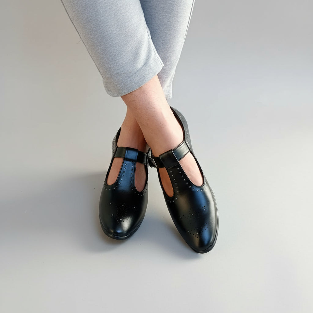 Black shoes with studded details worn by a person on a stone floor.