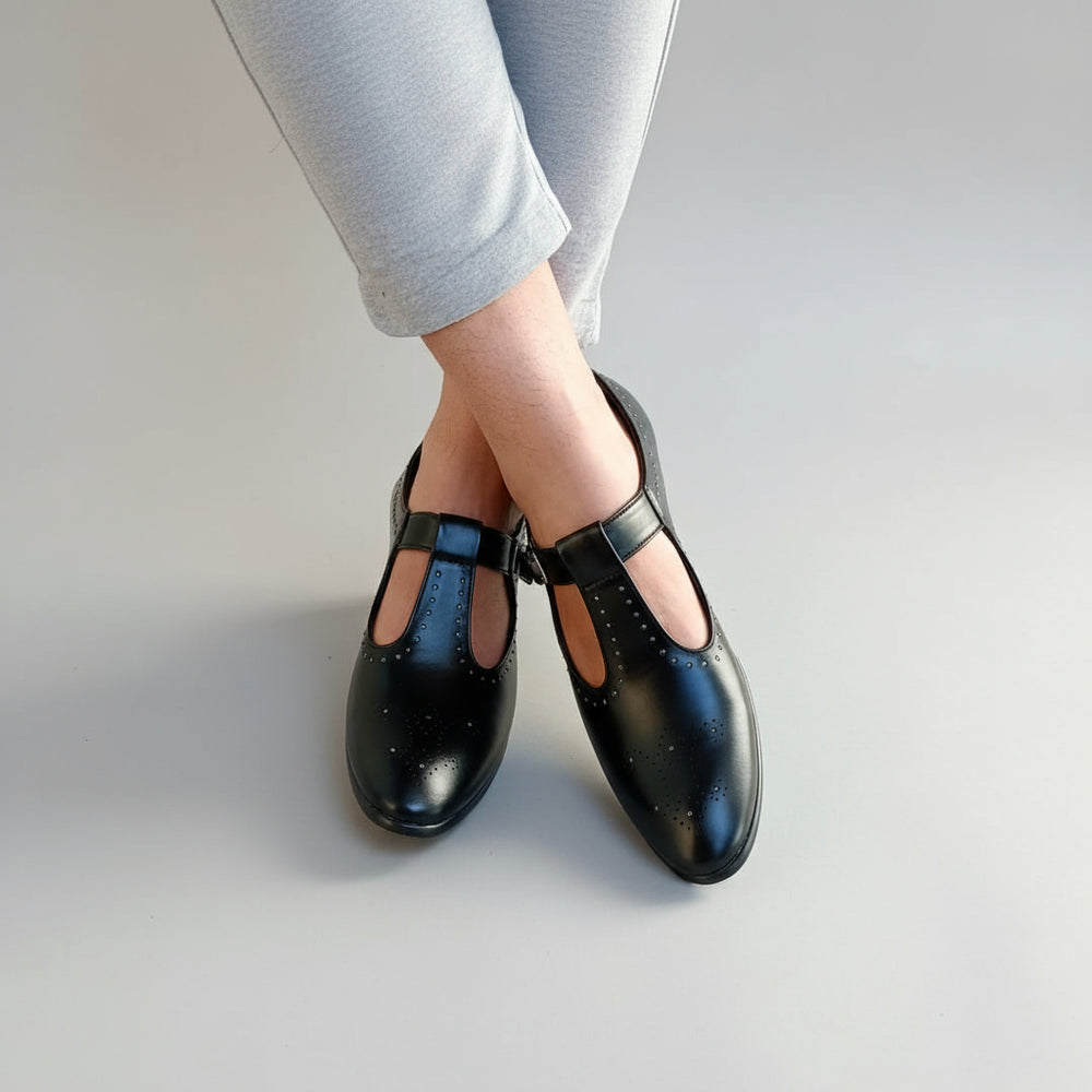 Black shoes with studded details worn by a person on a stone floor.