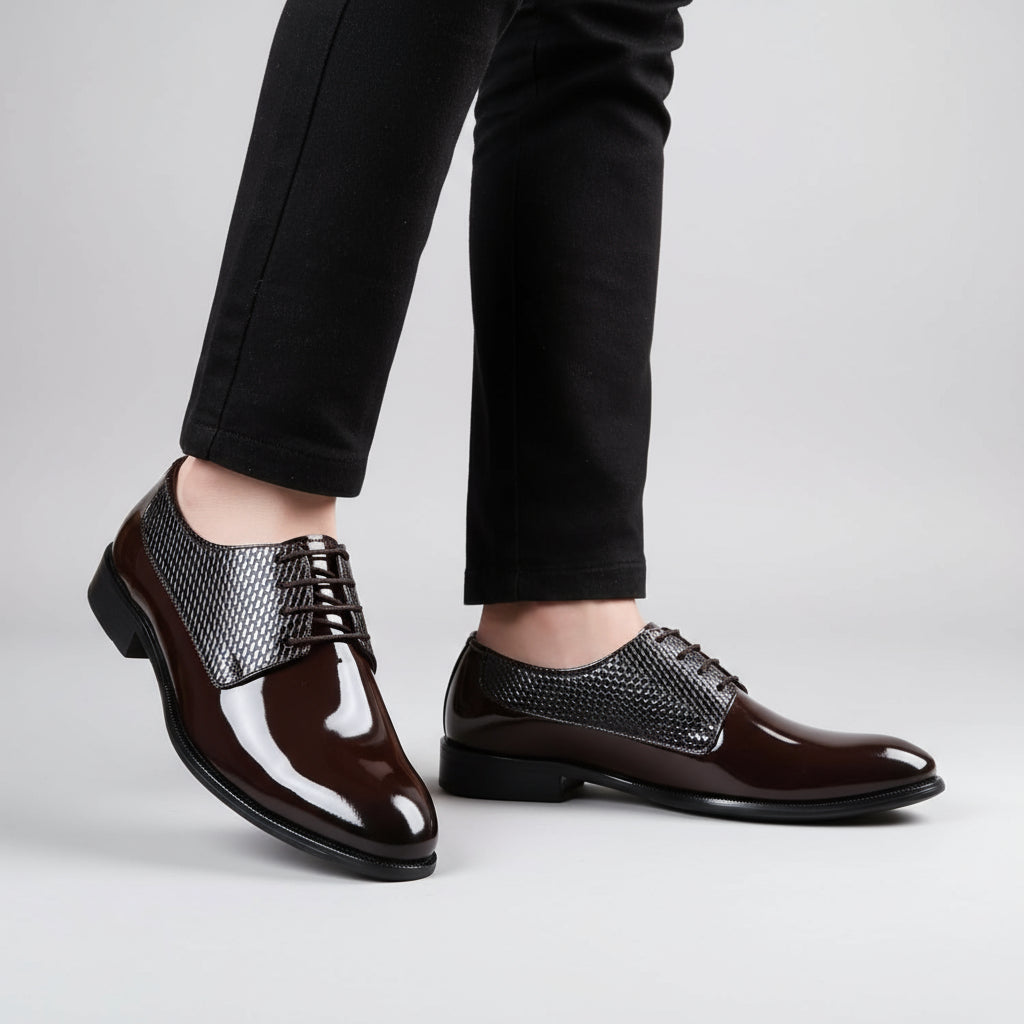 Brown dress shoes with patterned laces worn by a person on a wooden floor.