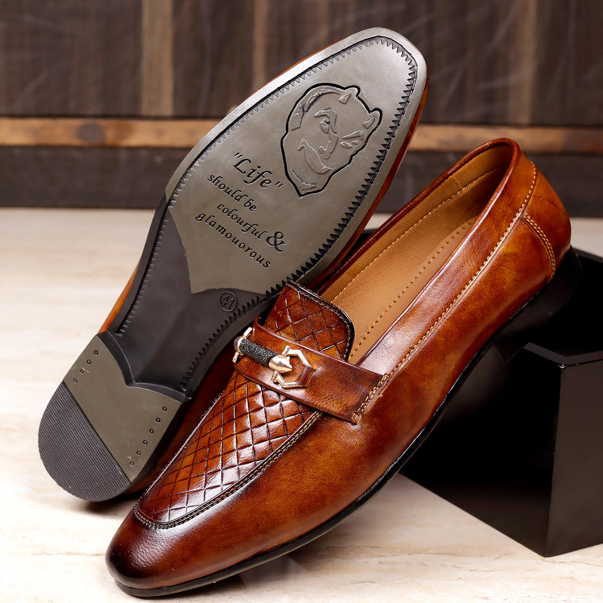 Brown leather loafer shoe with decorative buckle on a wooden surface