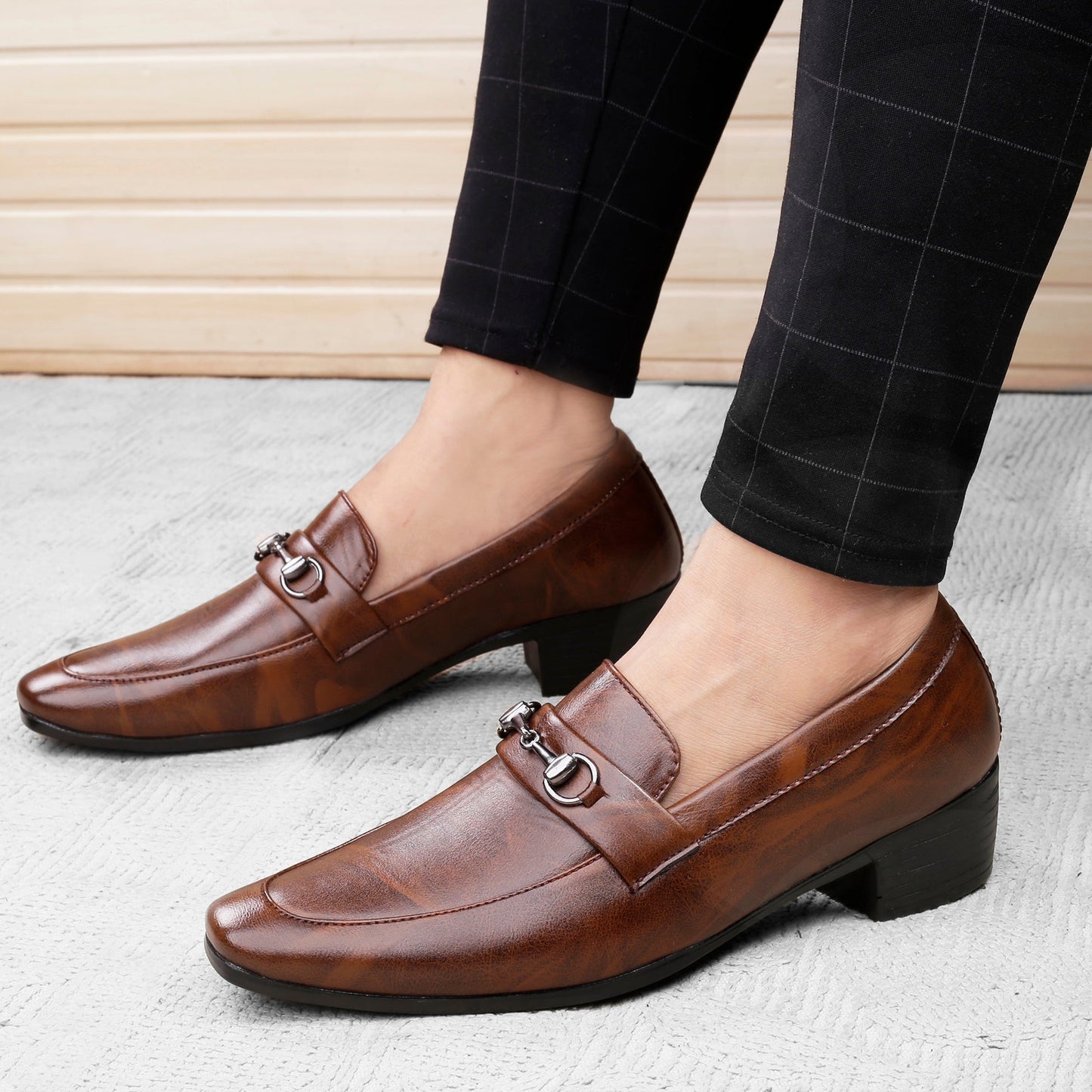Brown leather loafers worn with black checkered pants on a light background