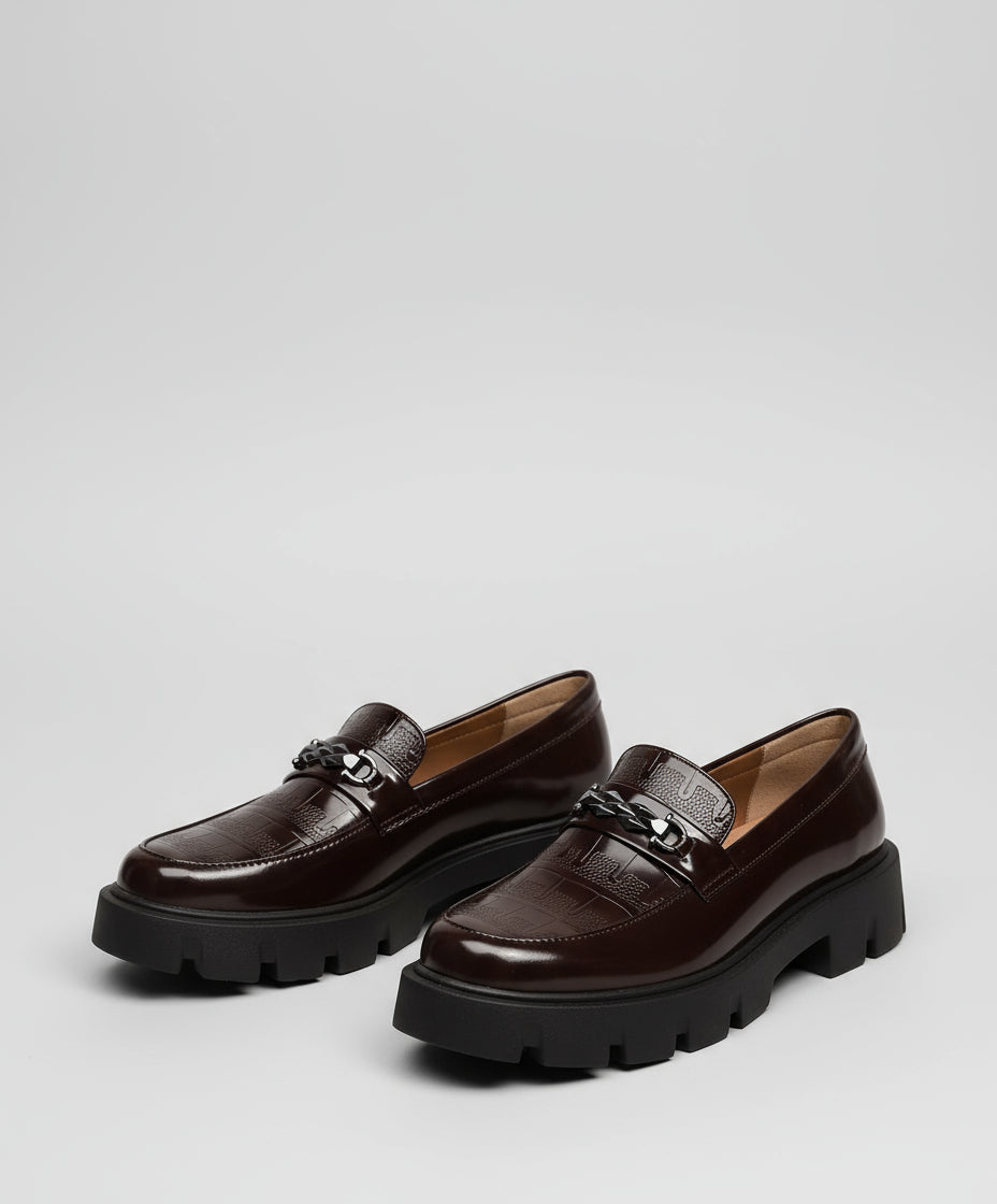 Brown leather shoes worn by a person sitting on a textured surface.