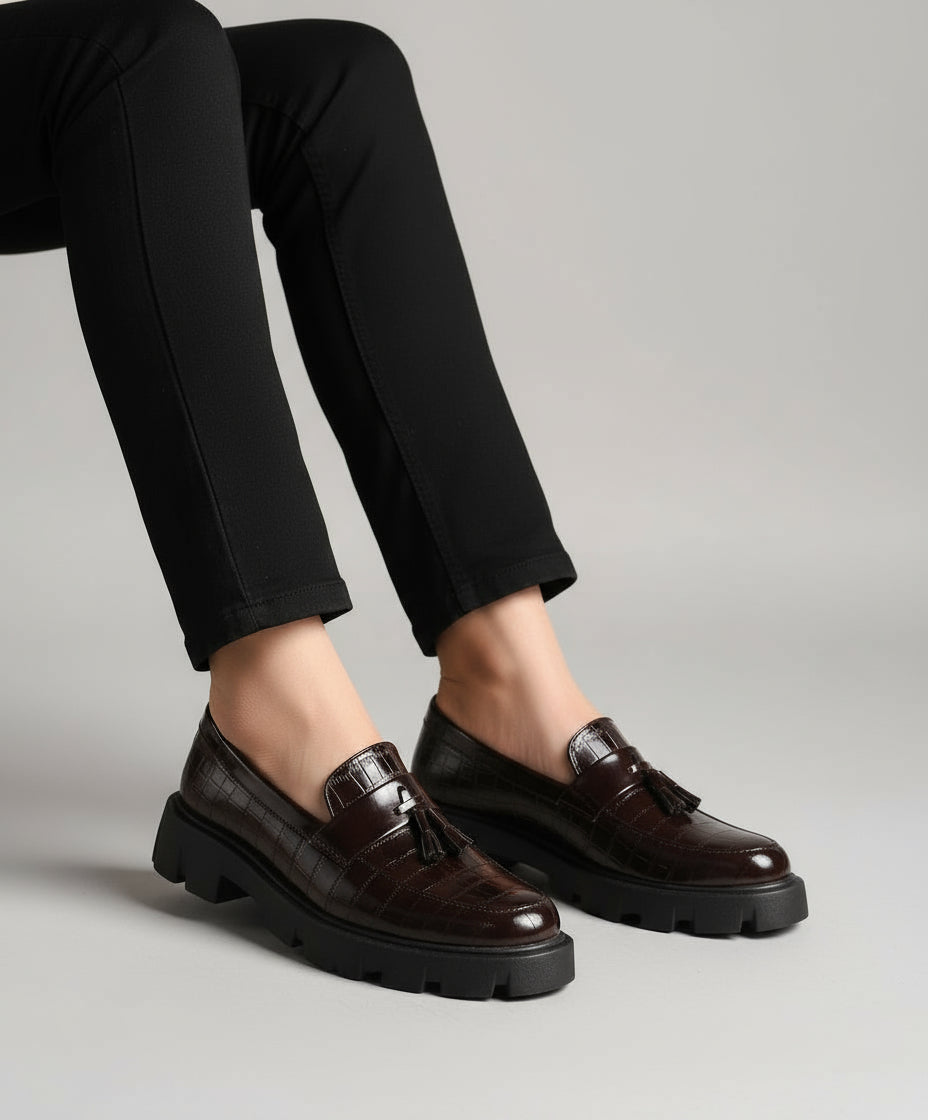 Brown leather shoes with tassels worn indoors on a textured surface.