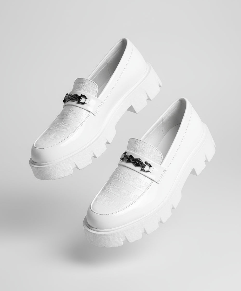 White loafers with a chain detail worn by a person sitting on a textured surface.