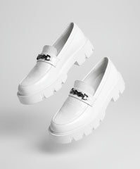 White loafers with a chain detail worn by a person sitting on a textured surface.