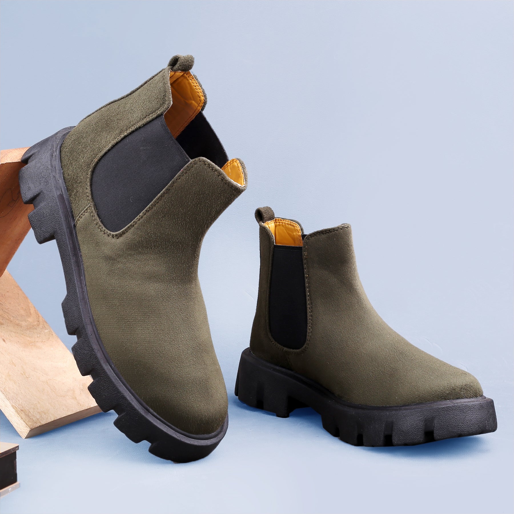 Green Chelsea boots with black soles on a light blue background