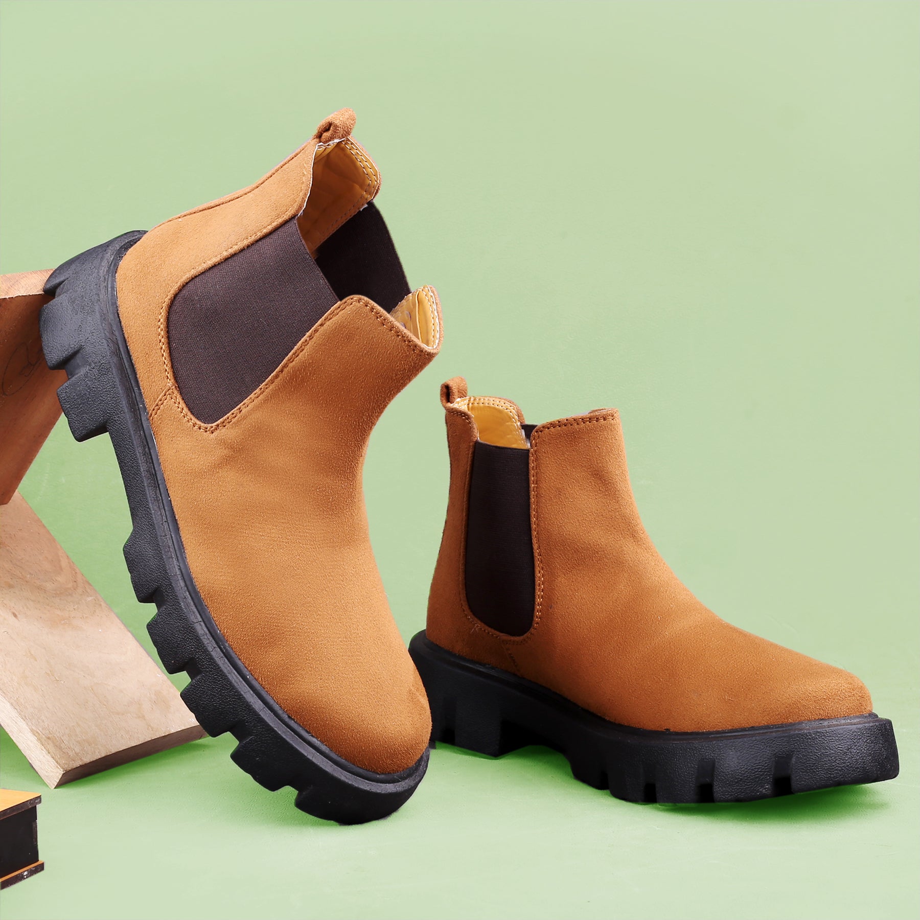 Brown Chelsea boots with black soles on a light green background
