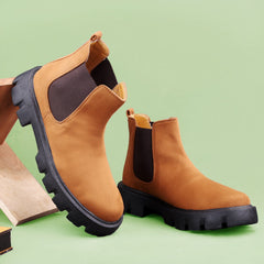Brown Chelsea boots with black soles on a light green background