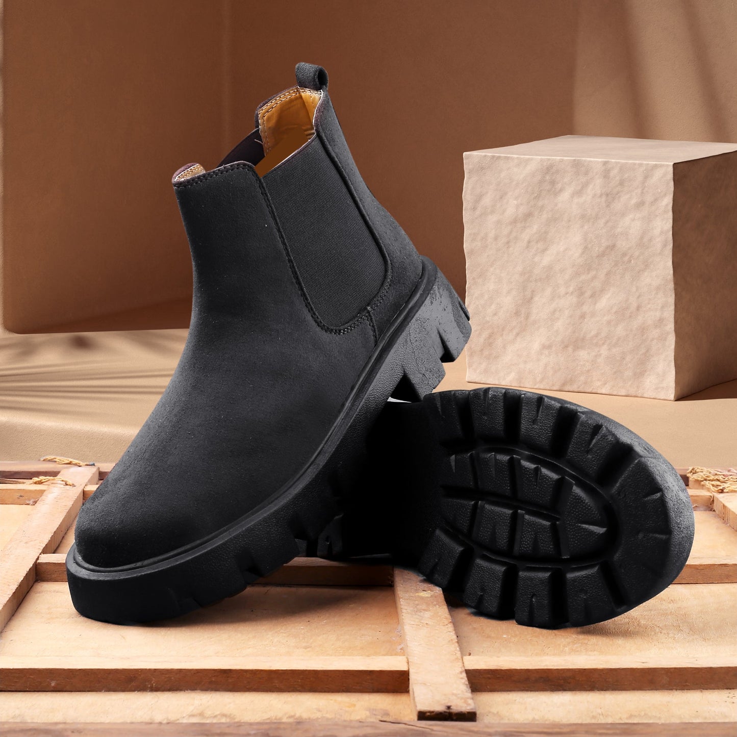 Black Chelsea boots on a wooden surface with a brown background