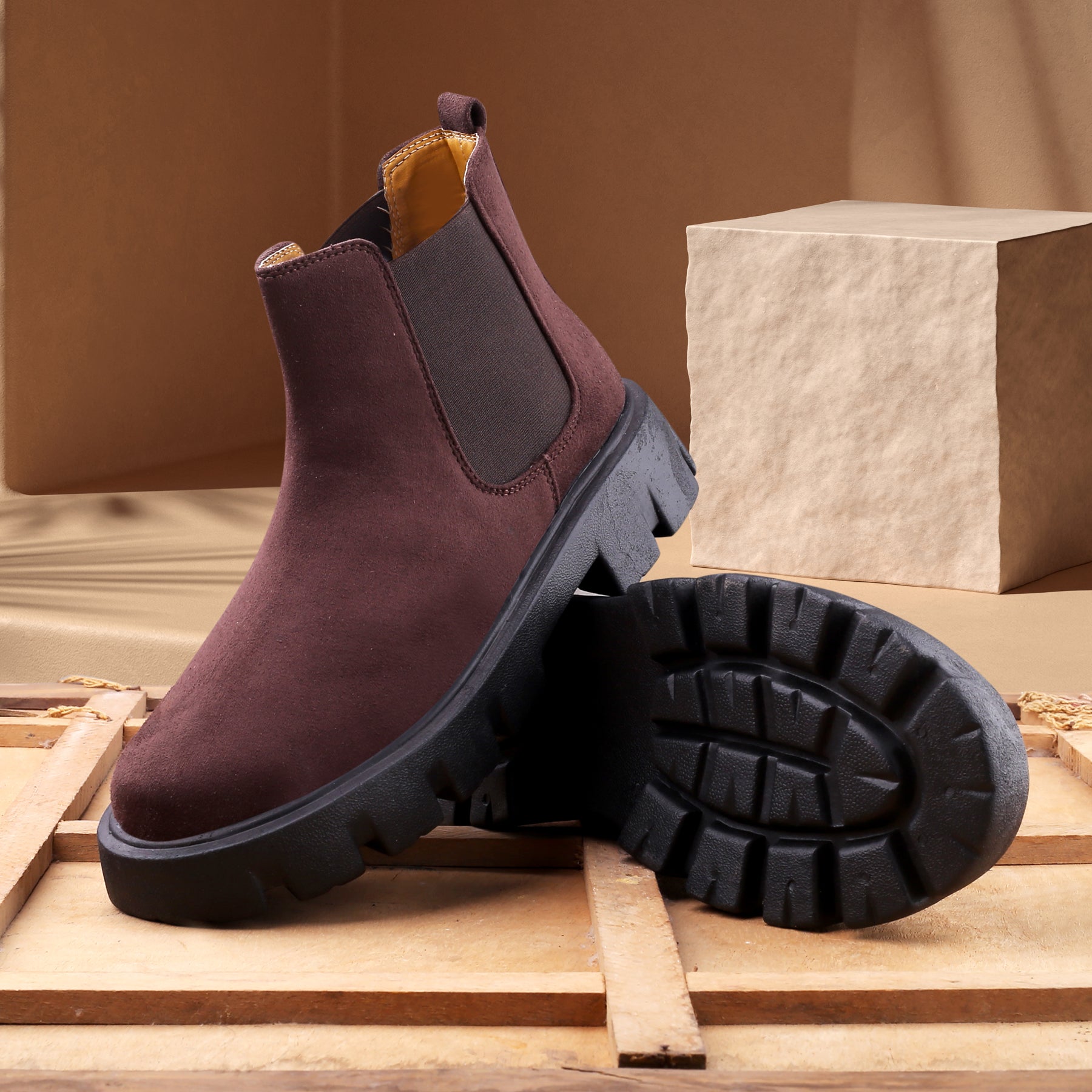 Brown Chelsea boots with black soles on a wooden surface
