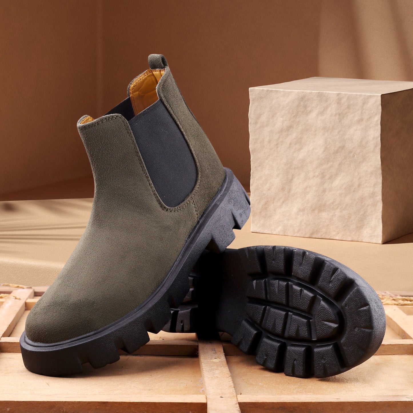 Green Chelsea boots with black soles on a wooden surface