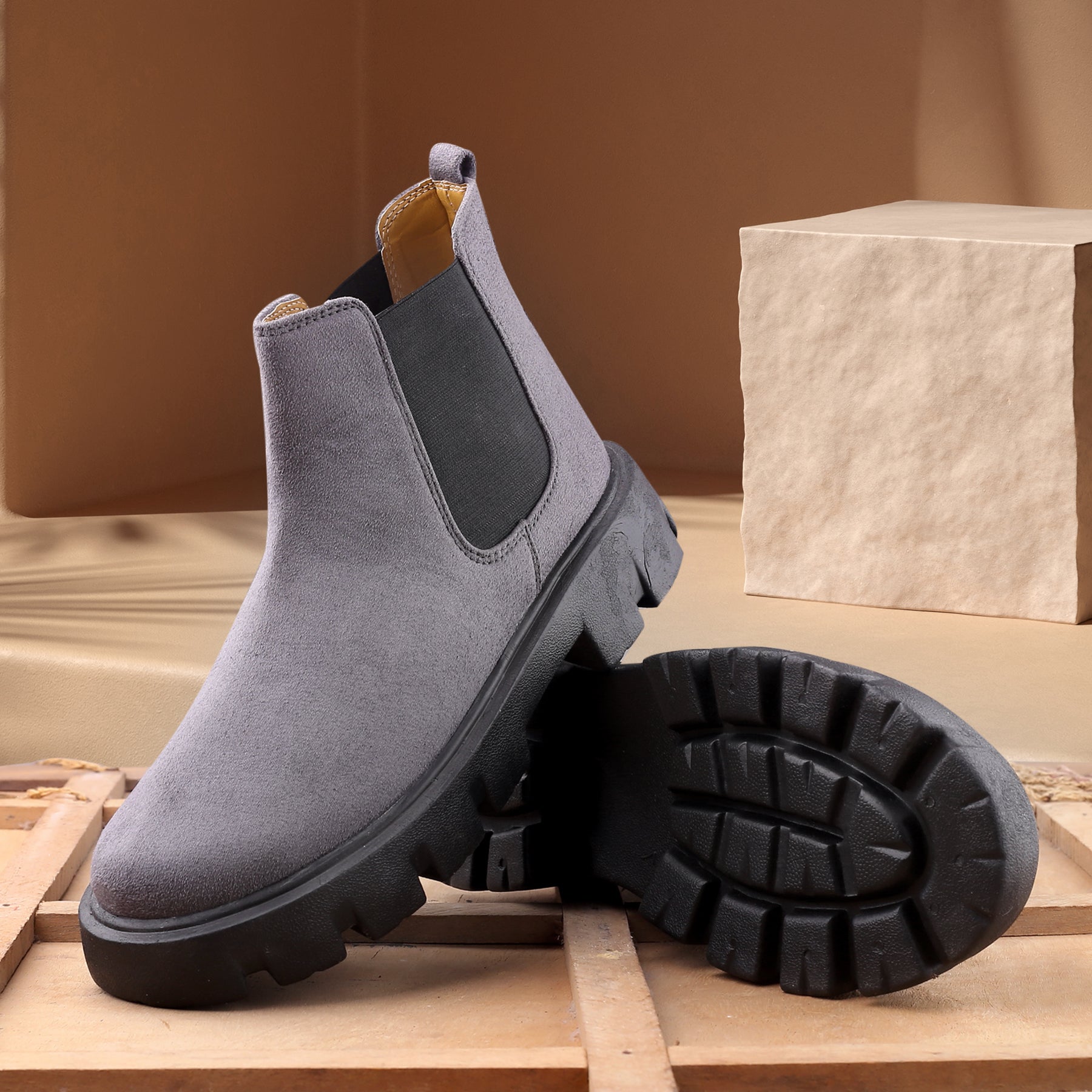 Gray suede Chelsea boots with black soles on a wooden surface.