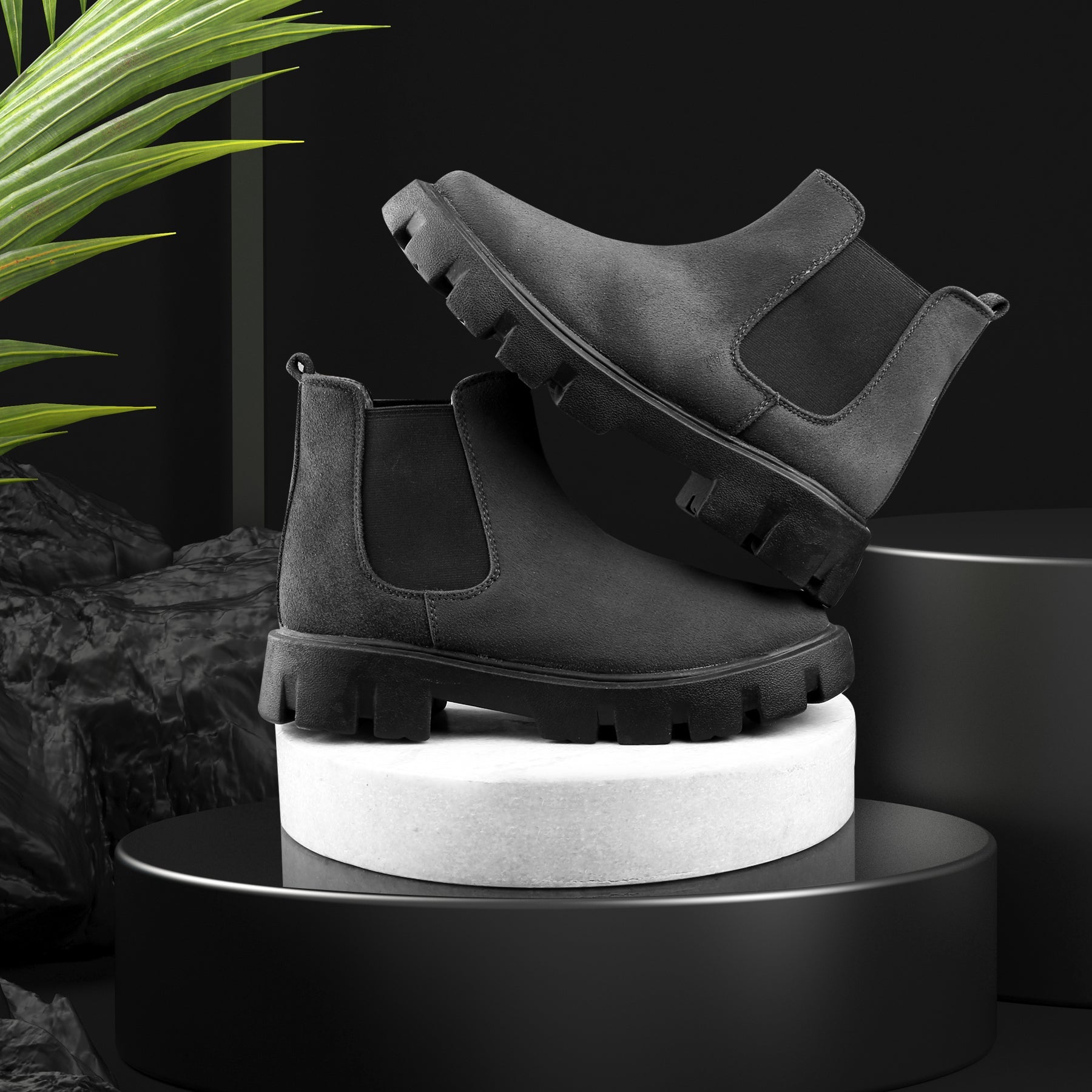 Black Chelsea boots on a white cylindrical stand with a dark background