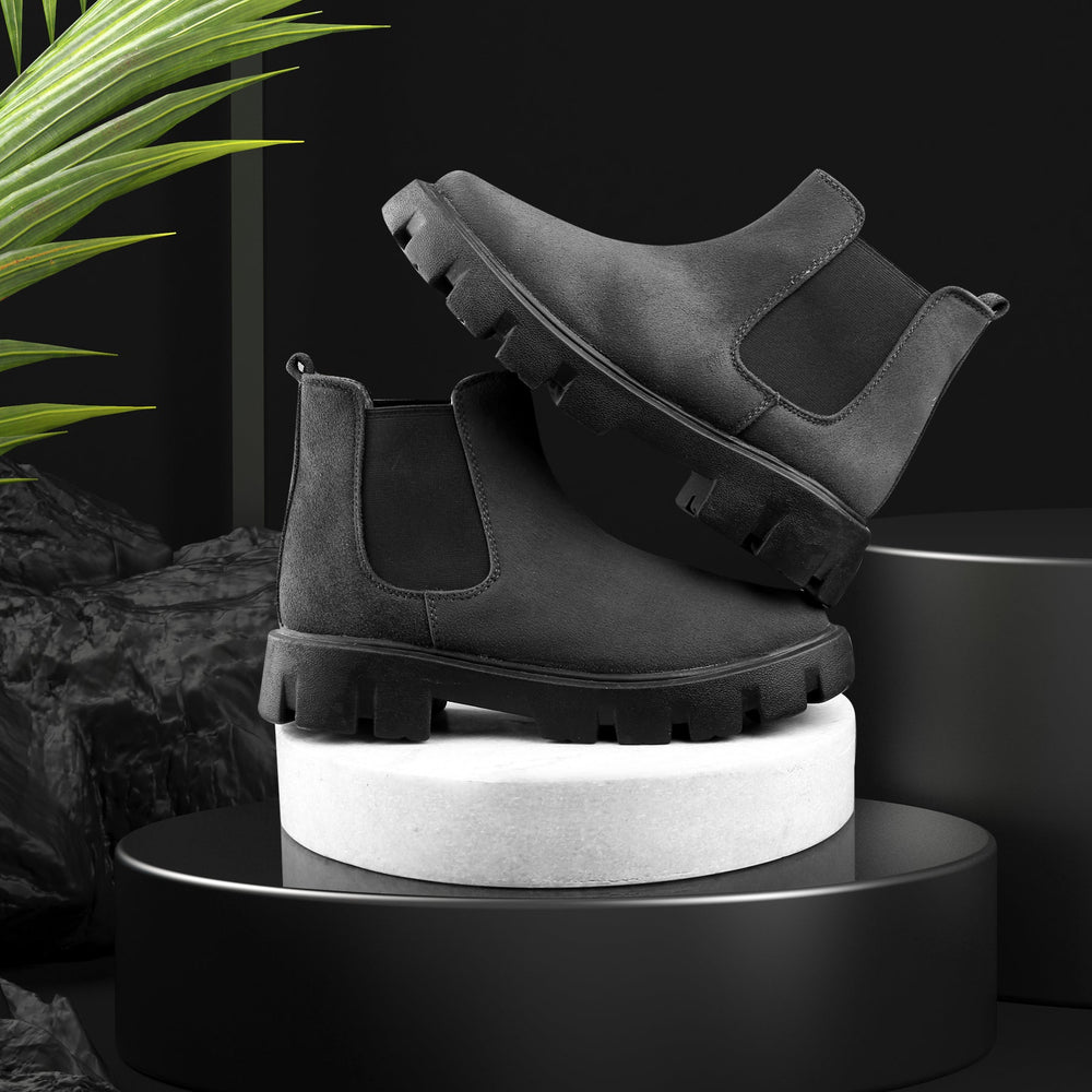 Black Chelsea boots on a white cylindrical stand with a dark background