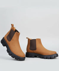 Brown boots with black soles worn by a person on a blurred outdoor background