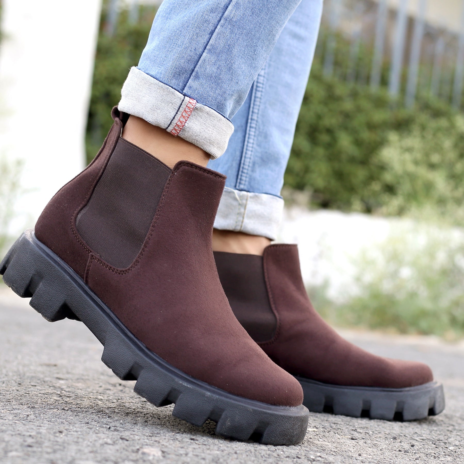 Brown Chelsea boots worn with rolled-up jeans on a blurred outdoor background